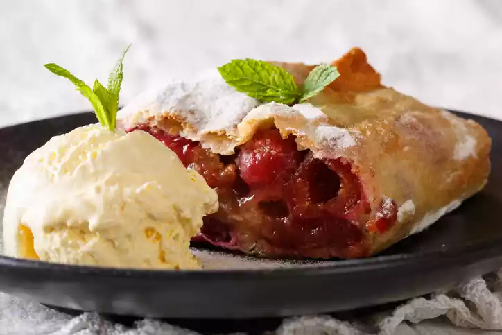 Homemade cherry strudel with powdered sugar and vanilla ice cream close-up